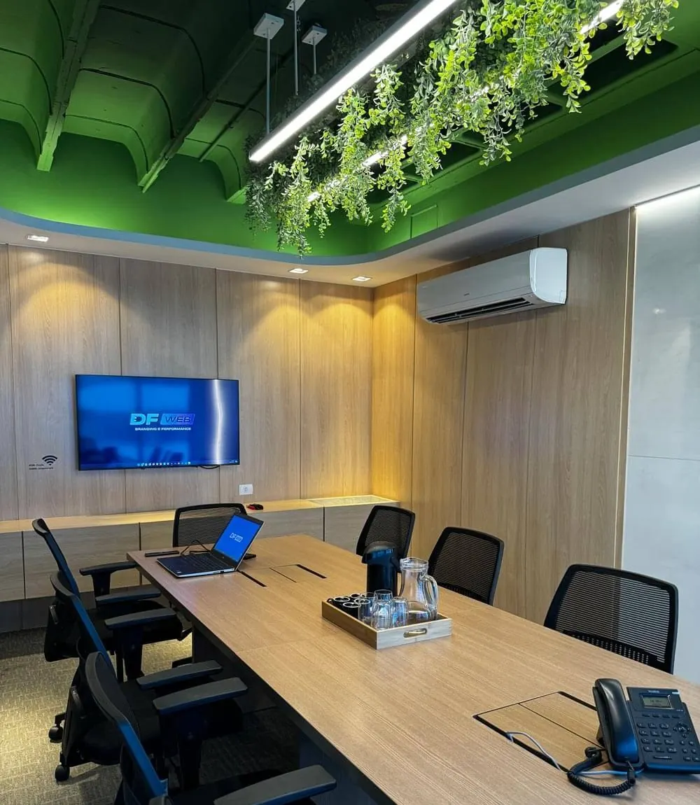 Sala de reunião da DFWeb em Icaraí, Niterói, com a marca na TV, mesa de madeira e jardim suspenso no teto
